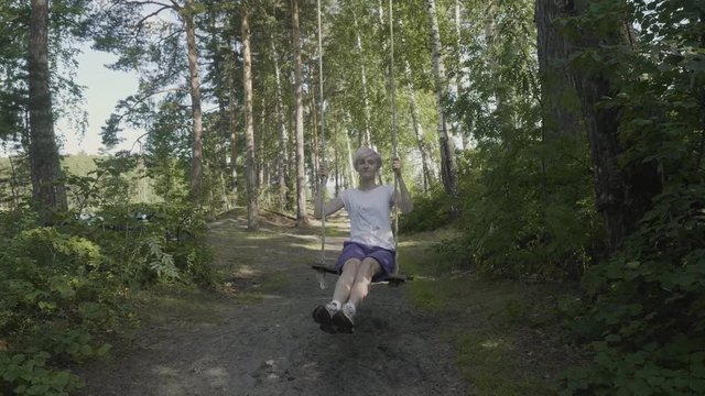Beautiful girl on the swing in the forest. Young woman rides a swing in the forest