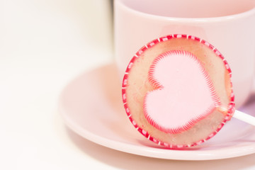 The concept of Love, Valentine's Day. A white coffee cup with a saucer and a pink candy with a heart, white background, close up