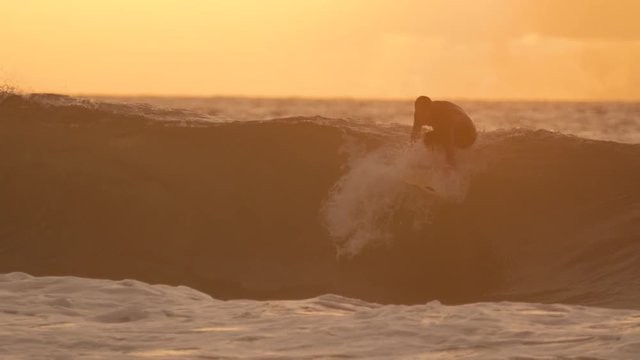 SLOW MOTION: Cool surfer stands up on his board and rides a tube wave at sunset. Unrecognizable man surfs awesome ocean wave on a picture perfect summer evening. Holiday recreation in touching scenery