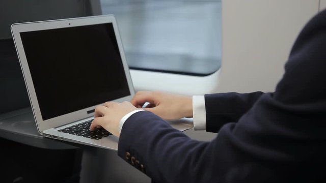 Male fingers of businessman print on laptop keyboard train. Man during travel on transport writes text and presses on touchpad on wireless computer.