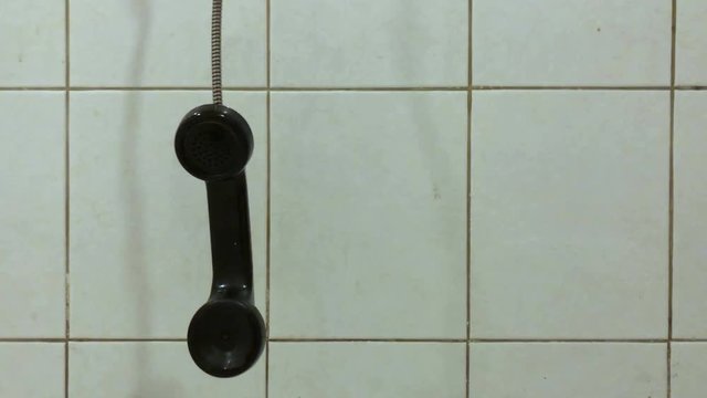 old pay phone handset dangling next to tile wall