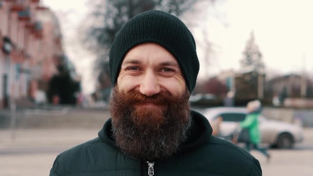portrait of a young bearded smiling man on the street, close-up