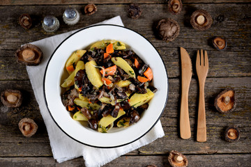 Stewed potatoes with onions, carrots and forest mushrooms on an old wooden background.