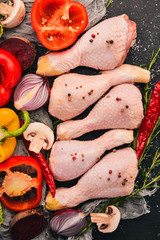 Raw chicken legs with fresh vegetables and rosemary and spices on a black wooden background. Top view. Free space for text.