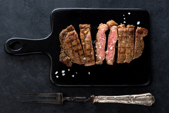 Slices beef Steak Ribeye on a black cutting board and meat fork