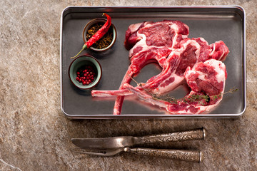 Raw lmeat lamb chops in a metal tray on gray concrete background