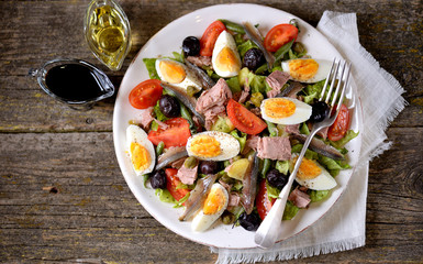 French salad Nicoise with tuna, boiled potatoes, egg, green beans, tomatoes, dried olives, lettuce and anchovies.
