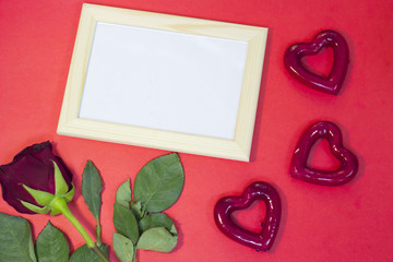 The concept of St.Valentine's Day with a beautiful red rose and wooden photo frame, red background, top view