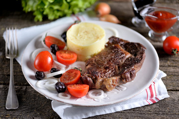 Beef steak with mashed potatoes and salad of cherry tomatoes, dried olives and white onions.