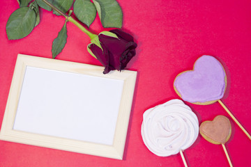 The concept of St.Valentine's Day with a beautiful red rose, wooden photo frame and ginger cookies on sticks, red background, top view