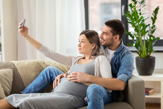 man and pregnant woman taking selfie at home