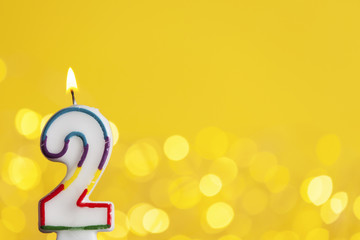 Number 2 birthday celebration candle against a bright lights and yellow background