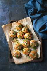 Traditional ukrainian homemade garlic buns pampushki for borscht soup with oil and coriander on old oven tray with baking paper over dark blue texture background. Top view, space
