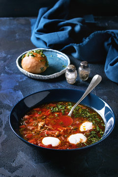 Plate of traditional beetroot borscht soup with sour cream and fresh coriander served with garlic bread buns pampushka with blue textile over dark blue texture background. Top view, space