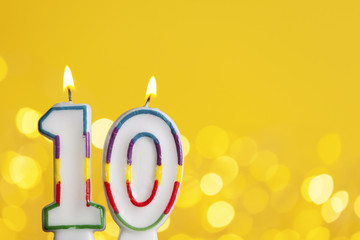 Number 10 birthday celebration candle against a bright lights and yellow background