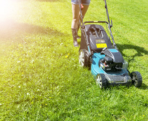 Beautiful girl cuts the lawn. Mowing lawns. Lawn mower on green grass. mower grass equipment. mowing gardener care work tool close up view sunny day. Soft lighting