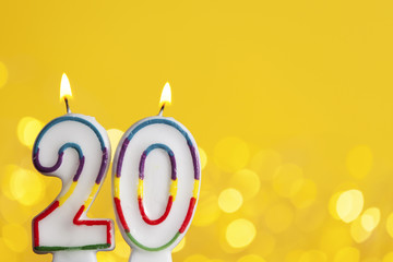 Number 20 birthday celebration candle against a bright lights and yellow background
