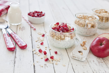 Ready-made healthy breakfast - muesli or granola with pomegranate, chia seeds and fresh natural yoghurt on white rustic wooden background, top view