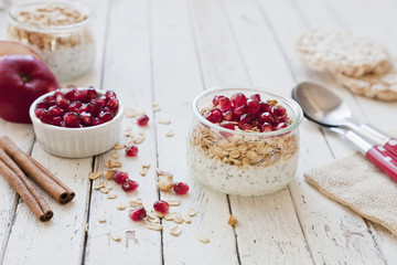 Ready-made healthy breakfast - muesli or granola with pomegranate, chia seeds and fresh natural yoghurt on white rustic wooden background, top view