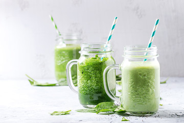 Variety of three color green spinach kale apple yogurt smoothie in mason jars with retro cocktail tubes over gray background. Healthy vegan detox eating.