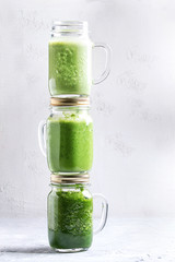 Variety of three color green spinach kale apple yogurt smoothie in mason jars on each other over gray background. Healthy vegan detox eating.