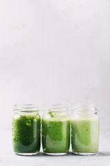 Variety of three color green spinach kale apple yogurt smoothie in mason jars in row over gray background. Healthy vegan detox eating. Toned image