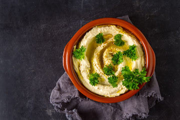 Vegetarian snack. Hummus with greens, dressed with olive oil and paprika in a ceramic plate. Dark background. Traditional Middle Eastern cuisine. 