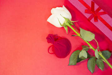 The concept of St.Valentine's Day with a beautiful white rose and a gifts in a box and in a suede bag, top view, copy space