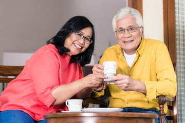 Portrait of serene senior couple looking at camera while enjoying a cup of coffee at home