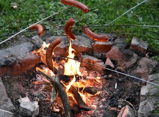 tourists roast sausages in nature over a fire in a stone fireplace