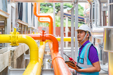 Asian engineer wearing glasses working in the boiler room,maintenance checking technical data of heating system equipment,Thailand people