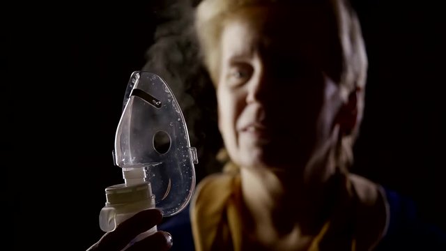 elderly woman is looking on a steam inhaler for treatment of respiratory diseases,bringing to face
