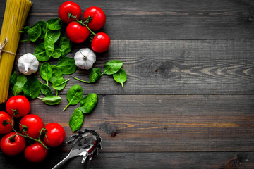 Main ingredients for italian pasta. Spaghetti, tomatoes, garlic, green basil on dark wooden background top view copy space