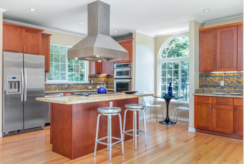 Kitchen in luxury home with stainless steel appliances, granite work surfaces, bar stools and wooden floor.