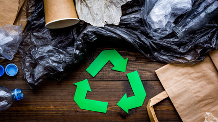 Green paper recycling sign among waste materials paper, plastic, polyethylene on dark wooden...