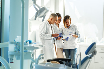 Medical dentist team in dental office discuss about practice and examining list of patients. - Powered by Adobe