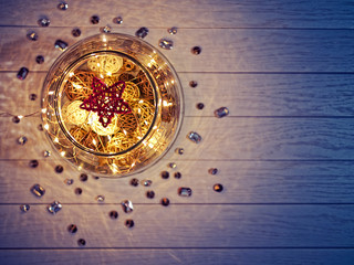 The woven figure of the star is inside a large glass ware on a wooden background. Under the star there are wicker balls and a luminous garland. Around the vase are the crystals.