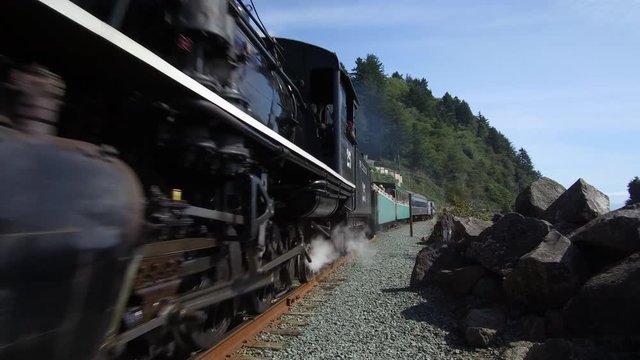 Locomotive steam train rides past camera on tracks, with audio of bell and engine. ProRes file, shot in 4K UHD.