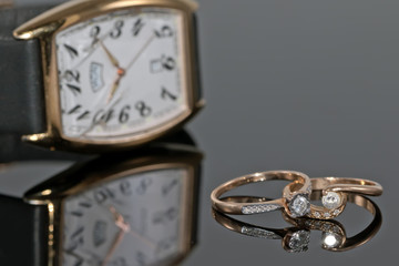 Pair of women's gold rings with diamonds on a background of elegant watches