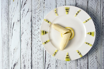 Banana, kiwi, lemon in the form of a clock on a white plate
