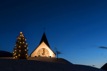Cute little chapel with lightened christmas tree under clear sky at night