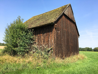 Obraz premium An old wooden granary in fall with dry weeds and grass in the foreground and a harvested field in the background