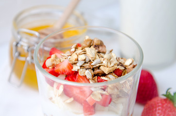 Top view healthy breakfast of homemade granola cereal with milk, strawberry, nuts and fruit, honey with drizzlier on white background. Morning food, Diet, Detox, Clean Eating, Vegetarian concept.