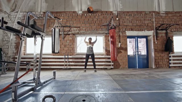 Zoom in of strong woman doing squats and throwing upwards medicine ball during cross training workout