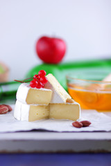 Camembert with green grapes, honey with brie cheese, green bottle in the background, red berries and pink flower, peanuts, healthy food, French breakfast with brie cheese