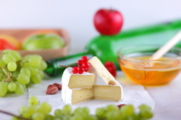 Camembert with green grapes, honey with brie cheese, green bottle in the background, red berries and pink flower, peanuts, healthy food, French breakfast with brie cheese