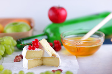 Camembert with green grapes, honey with brie cheese, green bottle in the background, red berries and pink flower, peanuts, healthy food, French breakfast with brie cheese