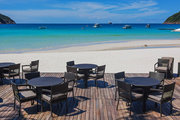 Wattled tables and chairs on wooden terrace in cafe on paradise beach with white sand and turquoise...