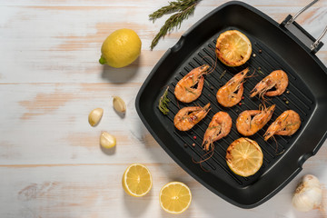 Grilled shrimps on a grill frying pan with lemon, paprika, spices and herbs. Wooden background.