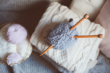 Grey and pink Yarn ball with knitting needles in metallic basket with knitted sweaters on background. Hobby, cozy homely weekend and hugge concept.